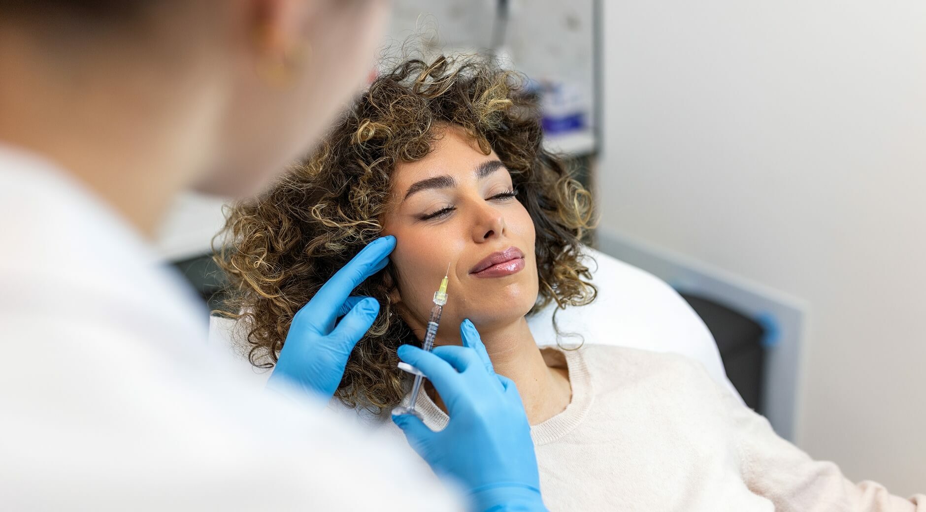 Woman receiving Restylane dermal filler injection to cheek from provider in blue gloves during aesthetic treatment